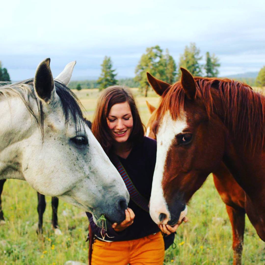 A white person with long auburn hair rests their chin on the face of a beautiful white horse, and gazes into their dark eyes.
